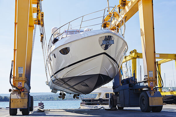 Rumpf- und Decksarbeiten bei IBH Yachtservice Kleines Motorboot wird an land von einem Kran getragen