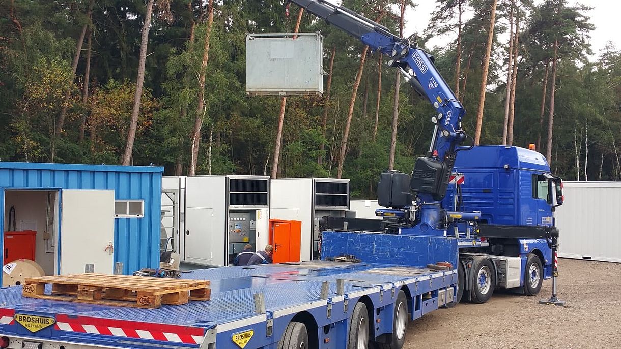 Lieferung und Inbetriebnahme durch die IBH vor Ort Blauer LKW mit Krahn bei der Anlieferung eines Aggregats